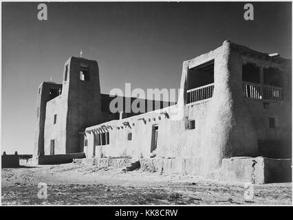 Eine schwarze und weiße Fassade Foto von San Estevan del Rey Mission Church, das Adobe Gebäude im 17. Jahrhundert gebaut wurde, Holzbalken, die die Struktur für das Dach schaffen ragen aus der Seite werden kann, mehrere Kreuze auf der Oberseite der Kirche und eine zweite Etage bacony gesehen werden kann im Vordergrund befindet, das Bild stammt aus einer Serie von Fotografien bekannt als Wandbild Projekt von Ansel Adams, er durch den National Park Service 1941 beauftragt wurde, eine fotografische Wandbild für das Ministerium des Innern in Washington DC zu erstellen, wird das Projekt zu einem Ende kam durch Stockfoto