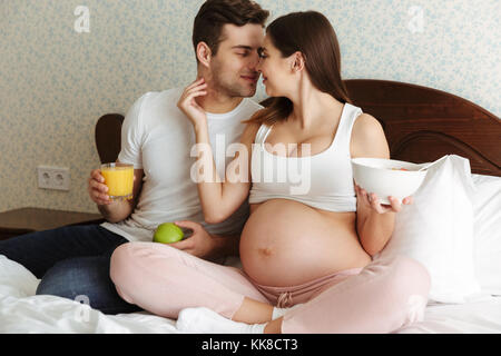 Porträt einer reizenden jungen schwangeren Paare in gesundes Frühstück zusammen, während Sie im Bett sitzen, Stockfoto