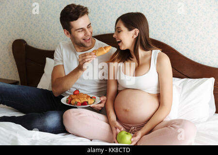 Porträt einer fröhlichen jungen schwangeren Paar gesundes Frühstück zusammen, während Sie im Bett sitzen Stockfoto