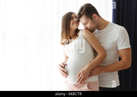 Foto von stattlicher Mann Hug seine reizende schwangere Frau zuhause zu Hause und Küssen. Stockfoto
