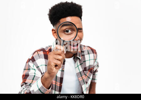Porträt einer fröhlichen jungen afrikanischen Mann durch Lupe auf weißem Hintergrund suchen Stockfoto