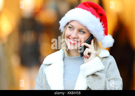 Glückliche Frau tragen Klausenmütze Anruf auf dem Mobiltelefon in Weihnachten auf der Straße in einem kommerziellen Zentrum Stockfoto