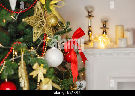 Geschmückten Weihnachtsbaum. Hintergrund für den Urlaub. rot, gold und weiße Kugeln auf einem Zweig. Girlanden und Sterne, eine große rote Schleife. Im Hintergrund einer Stockfoto