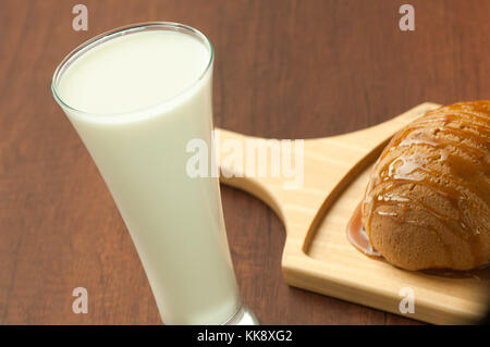 Brot mit Honig beträufelt auf einer hölzernen Platte und ein Glas Milch Stockfoto