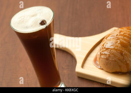 Brot mit Honig beträufelt auf einer hölzernen Platte und einem Glas Cocktail mit Beeren Stockfoto