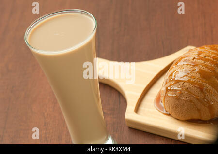 Brot mit Honig beträufelt auf einer Holzplatte und ein Glas Milchshake Stockfoto