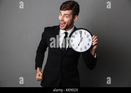 Glücklich verlassen bärtiger Mann im schwarzen Anzug Holding, an der Kamera suchen, auf grauem Hintergrund Stockfoto
