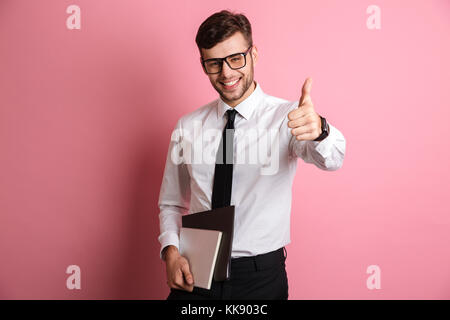 Portrait Of Happy attraktiver Mann in weißem T-Shirt und Brillen holding Dokumente beim Stehen und zeigen den Daumen oben-Geste über rosa Bac isoliert Stockfoto