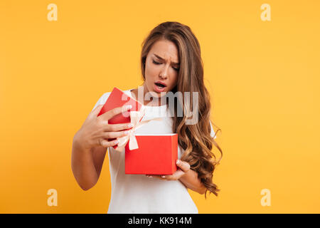 Portrait einer umgekippt enttäuscht Mädchen öffnen Geschenkbox über Gelb Hintergrund isoliert Stockfoto