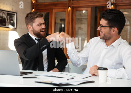 Zwei lustige bärtigen Kollegen in formale gelocht, während im Büro sitzen Stockfoto