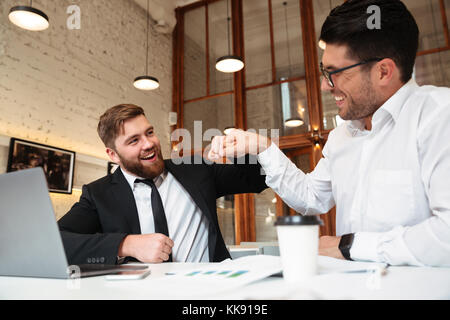 Zwei lächelnde bärtigen Kollegen in formale gelocht, während im Büro sitzen Stockfoto