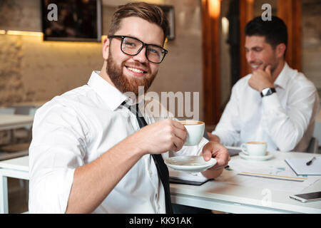 Porträt eines lächelnden bärtigen Geschäftsmann Kaffee trinken mit seinen männlichen Kollegen auf einem Hintergrund arbeiten Stockfoto