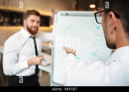 Zwei junge Unternehmer in einer Besprechung und Diskussion von Plan auf einer Tafel im Innenbereich Stockfoto