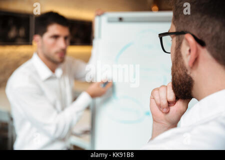 Zwei nachdenklich ernsten Unternehmer in einer Besprechung und Diskussion von Plan auf einer Tafel im Innenbereich Stockfoto