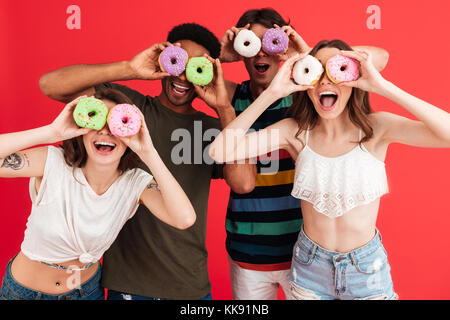 Porträt einer Glücklich lächelnde Gruppe der multirassischen Freunde im Sommer Kleidung Spaß beim gemeinsam mit Donuts über den roten Hintergrund isoliert Stockfoto