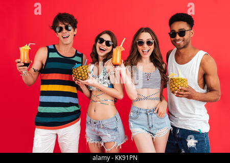 Gruppe von lächelnden Jungen multirassischen Freunde im Sommer Kleidung stehend mit tropischen Cocktails über den roten Hintergrund isoliert Stockfoto