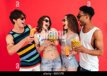 Gruppe der glückliche junge Multirassischen Freunde im Sommer Kleidung sprechen beim Stehen mit tropischen Cocktails über den roten Hintergrund isoliert Stockfoto