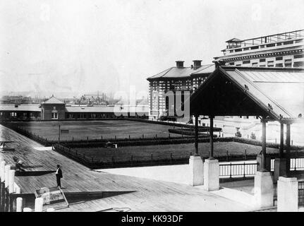 Ein Foto von einem Teil der Ellis Island Immigration Prüfplatz, der französischen Renaissance Revival Gebäude mit roten Ziegeln und Kalkstein Verkleidung konstruiert wird, das Gebäude wurde erstmals am 17. Dezember 1900 eröffnet, ist im Jahr 1954 war nach der Verarbeitung über 12 Millionen Einwanderer die Einreise in die Vereinigten Staaten geschlossen, die grossen überdachten Gehweg auf der rechten Seite des Fotos führt zum Haupteingang des Gebäudes, Rasen in sind mit Sträuchern außerhalb des Gebäudes eingezäunt, ein Mann gesehen werden kann, auf dem Wasser, New York, 1907. Von der New York Public Library. Stockfoto