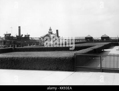 Ein Foto von der Pier auf Ellis Island, die Fähre angedockt auf der linken Seite des Bildes durch das Ministerium für Wirtschaft und Arbeit betrieben wurde, Sie die United States Immigration Services zwischen 1903 und 1913 betreute, Gebäude, die einen kleinen Teil der Strukturen, die auf Ellis Island machen kann im Hintergrund gesehen werden, Rasen, ummauerten durch scheuert sich durch große Gehwege umgeben sind, Ellis Island eröffnet 1892 und 1954 nach der Verarbeitung über 12 Millionen Einwanderer geschlossen, New York, 1907. Von der New York Public Library. Stockfoto