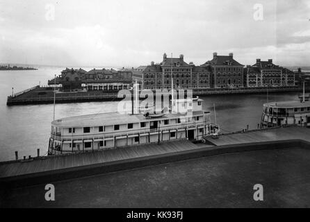 Schwarz-weiß Foto mit Blick auf zwei Fähren am Pier in den Vordergrund und Ellis Island Gebäude im Hintergrund, scheinbar von oben auf die Einwanderung Bahnhofsgebäude, von Edwin Levick, Ellis Island, New York, 1907. Von der New York Public Library. Stockfoto