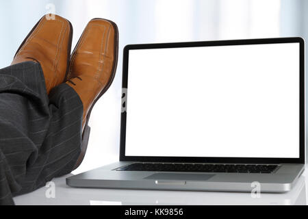 Geschäftsmann sitzt mit seinen Füßen auf dem Tisch neben einem Laptop mit weißer Bildschirm. Stockfoto