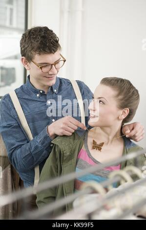 Junger Mann, der eine Halskette um den Hals einer jungen Frau im Modegeschäft legt | Nutzung weltweit, gebührenfrei: Für gewerbliche Nutzung Preis auf Anfrage. Stockfoto