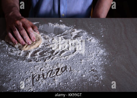 Mann, Küchenchef, Teig für Pizza mit Wort Pizza auf Mehl Stockfoto