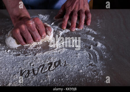 Mann, Küchenchef, Teig für Pizza mit Wort Pizza auf Mehl Stockfoto