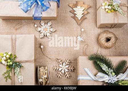 Klassische Weihnachten Geschenke präsentiert in braunem Papier mit Spielzeug und neue Jahr Dekor auf sackleinen. frohe Weihnachten Karte Hintergrund Stockfoto