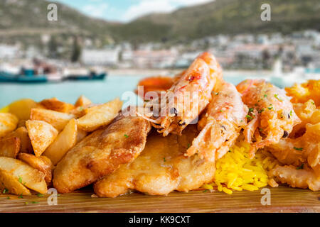 Fisch platter mit gebratenen Fische, Tintenfische und gegrillten Garnelen. als Beilage serviert Reis und Landwirt pommes Curry. Hintergrund zeigt einen malerischen fisherm Stockfoto