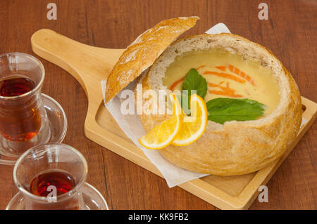 Hausgemachte Cremesuppe garniert mit Zitronenscheiben in einer Brot Schüssel auf dem Board und zwei Tassen schwarzen Kaffee Stockfoto