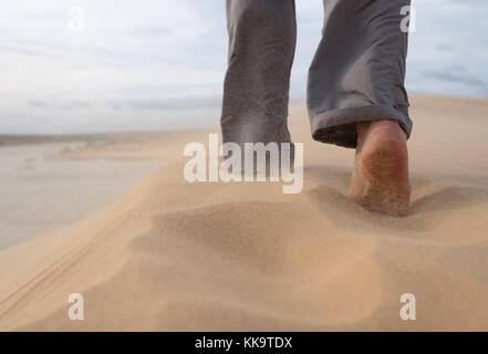Ein Mann Spaziergänge entlang der Sandstrand. In der Luft, der Sand fliegt von einem starken Wind. Stockfoto