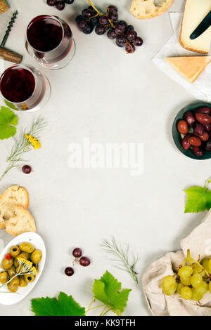 Wein- und Snackset. Verschiedene Käsesorten, Oliven, Prosciutto-Fleisch, Baguette-Scheiben, schwarze Trauben und Gläser Rotwein auf grauem Marmorboden, oben Stockfoto