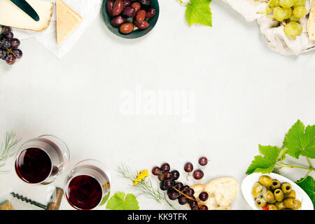 Wein- und Snackset. Verschiedene Käsesorten, Oliven, Prosciutto-Fleisch, Baguette-Scheiben, schwarze Trauben und Gläser Rotwein auf grauem Marmorboden, oben Stockfoto