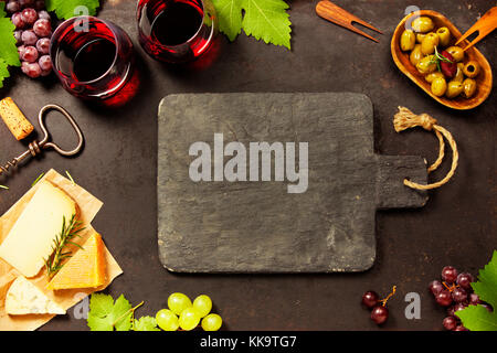 Wein und Snacks. Auswahl an Käse, mediterrane Oliven, Schwarze und grüne Trauben und Gläser Rotwein über dunklen Hintergrund, Ansicht von oben, kopieren Raum Stockfoto