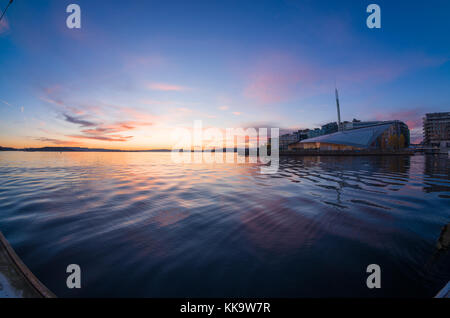 Uferpromenade von Tjuvholmen, Oslo, Norwegen, mit Astrup Fearnley Museum, unter farbenfrohem Sonnenuntergang, Blick vom schwimmenden Pier der Aker Brygge Marina. Stockfoto