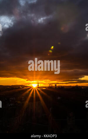 Edinburgh, Schottland, Vereinigtes Königreich. 29 Nov, 2017. Dramatischer Sonnenuntergang mit orange Sunburst über Edinburgh Skyline auf der Dachterrasse mit Lens flare in die dunklen Wolken und Silhouetten von kirchtürmen Stockfoto