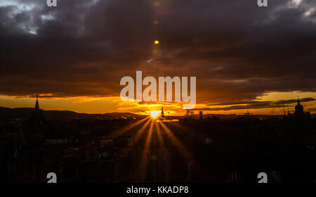 Edinburgh, Schottland, Vereinigtes Königreich. 29 Nov, 2017. Dramatischer Sonnenuntergang mit orange Sunburst über Edinburgh Skyline auf der Dachterrasse mit Lens flare in die dunklen Wolken und Silhouetten von kirchtürmen Stockfoto