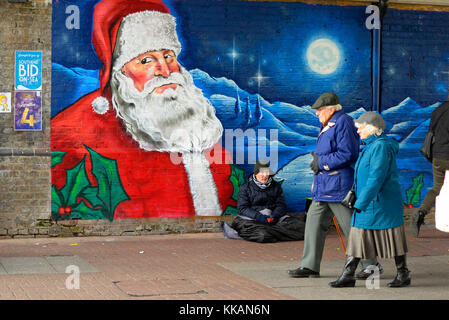 Obdachloser in Southend on Sea, die eingebrannte Obdachlosen-on-Sea. Rough sleeper, die in der Nähe von Frost neben Santa Claus Street Art. ältere Rentner vorbei gehen. Stockfoto