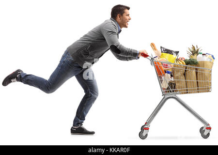 Volle Länge Profil geschossen von einem Kerl läuft und treibt einen Warenkorb mit Lebensmitteln auf weißem Hintergrund gefüllt Stockfoto