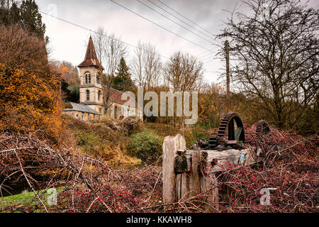 Gusseisen Zahnräder von Belvedere Mühle, mit Christus Kirche, chalford hinter, in der Nähe von Stroud, in den Cotswolds, Gloucestershire, England. Stockfoto