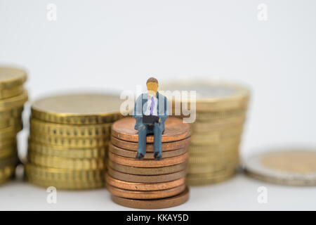 Miniatur Leute sitzen auf Münzen stapeln. auf weißem Hintergrund. Stockfoto