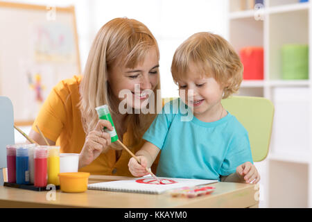 Kind malen im Kindergarten. Lehrer Hilfe von kleinen Jungen. Stockfoto