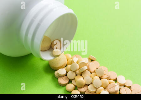 Haufen beige Kapseln am grünen Tisch. Flasche auslaufen Tabletten. Stockfoto