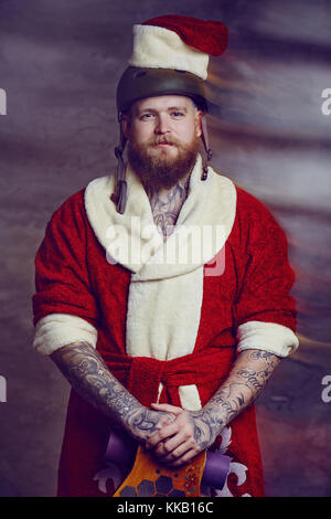 Ein Mann in santa Kleidung hält Longboard. Stockfoto
