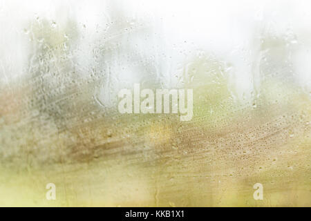 Makro Nahaufnahme des nassen Auto Glas Fenster mit Regen stürmisches Wetter, grüne unscharfen Bäume Wald im Herbst Stockfoto