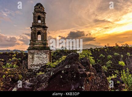 Der Turm der Kirche San Juan Parangaricutiro, der bei Sonnenuntergang aus einem Meer aus getrocknetem Lavagestein im abgelegenen Dorf San Juan Parangaricutiro, Michoacan, Mexiko, aufsticht. Diese Kirche ist die einzige noch verbliebene Struktur, die beim achtjährigen Ausbruch des Vulkans Paricutin begraben wurde, der 1943 zwei Dörfer verzehrte und die Region mit Lava und Asche bedeckte. Stockfoto