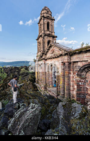 Touristen schallen um den Kirchturm von San Juan Parangaricutiro, der aus einem Meer aus getrocknetem Lavagestein im abgelegenen Dorf San Juan Parangaricutiro, Michoacan, Mexiko, aufsticht. Diese Kirche ist die einzige noch verbliebene Struktur, die beim achtjährigen Ausbruch des Vulkans Paricutin begraben wurde, der 1943 zwei Dörfer verzehrte und die Region mit Lava und Asche bedeckte. Stockfoto