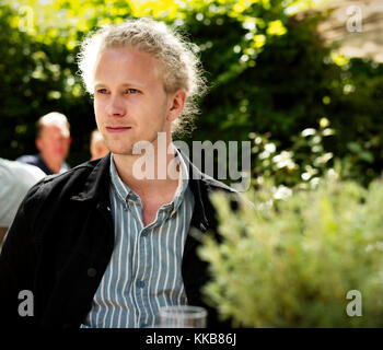 Junge blonde Mann an ein Restaurant im Freien, in einem Garten mit grüner Umgebung Stockfoto