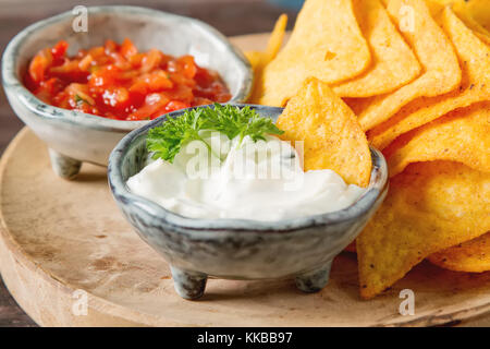 Snack für eine Partei, Chips mit einer Tortilla, Nachos mit Saucen: Salsa mit Tomaten, saure Sahne. mexikanisches Essen. dunklen Hintergrund. kopieren. Stockfoto